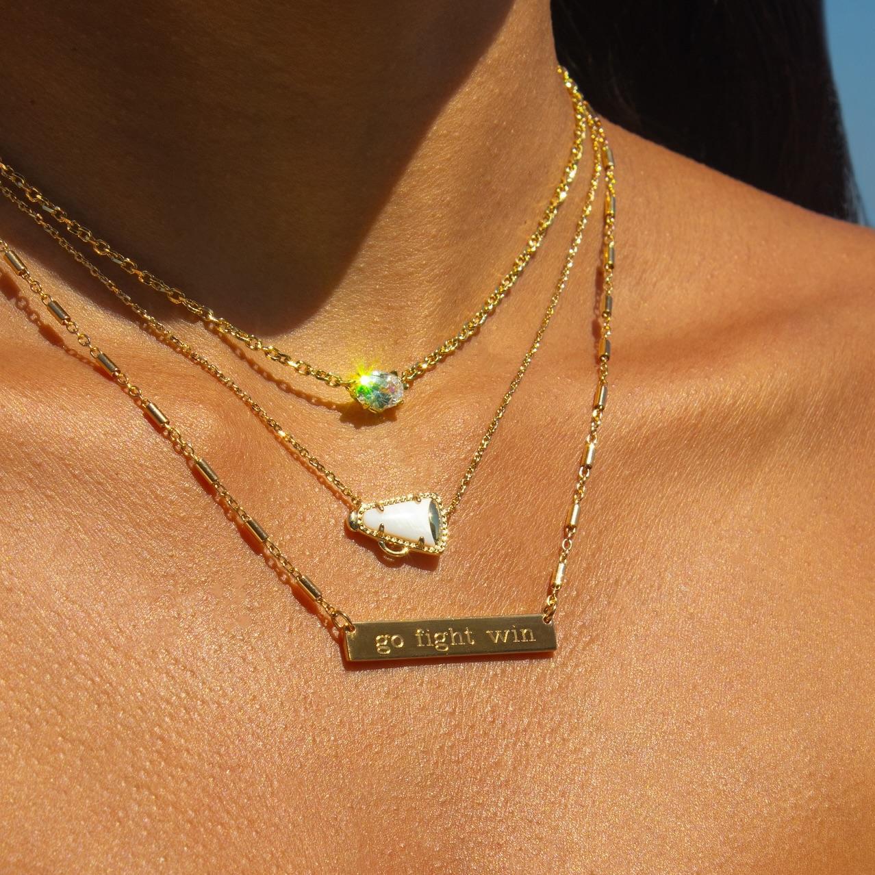Gold necklaces with gemstones and a bar necklace on a person's neck