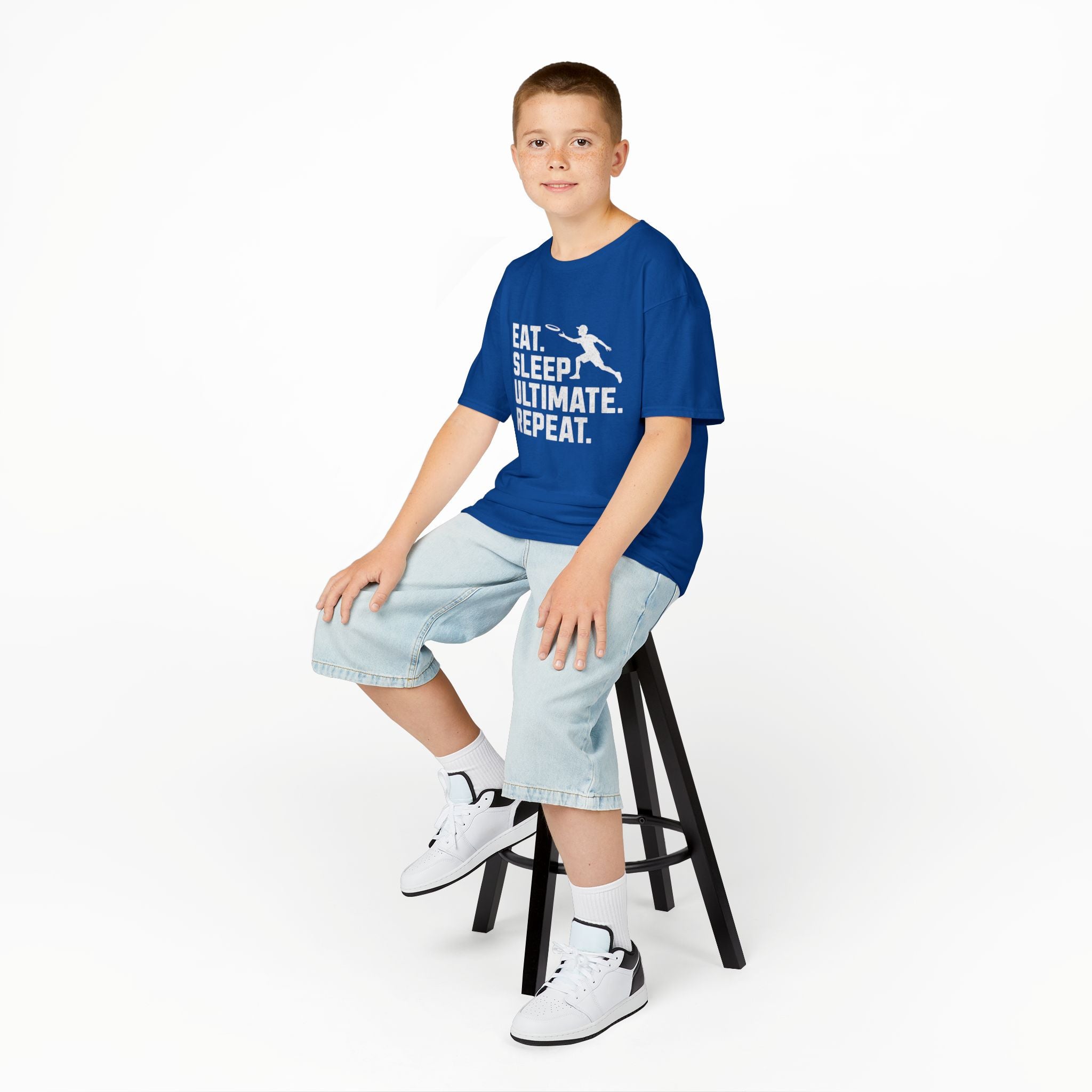 Child sitting on a stool wearing a blue t-shirt with text, on a white background