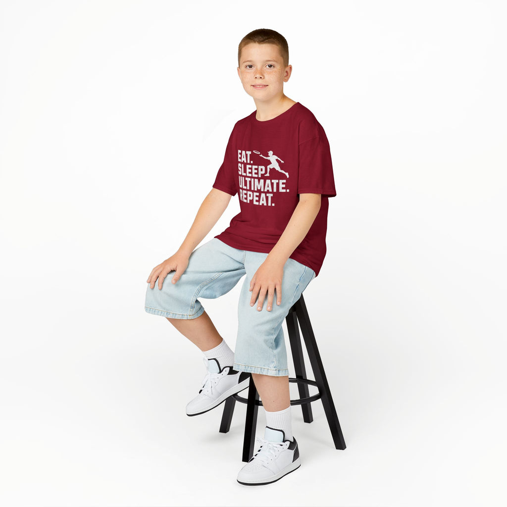 Child sitting on a stool wearing a red t-shirt with text and light blue shorts on a white background