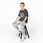 Child wearing a t-shirt with a cat graphic sitting on a stool against a white background