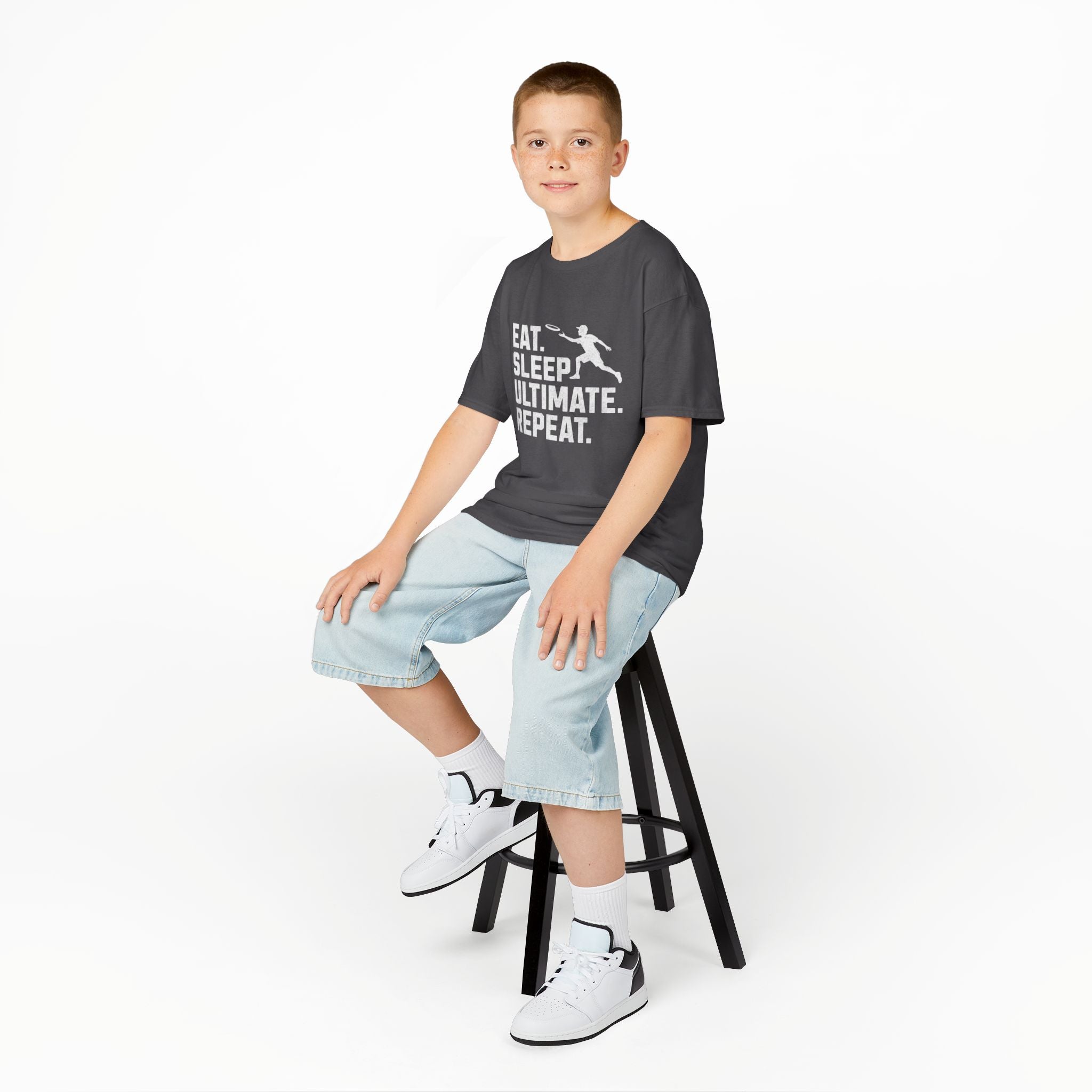 Child wearing a t-shirt with a cat graphic sitting on a stool against a white background