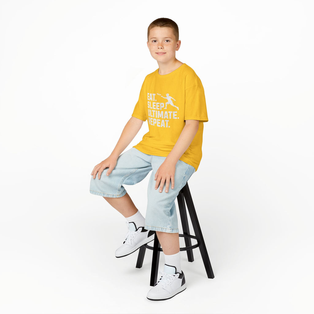 Child sitting on a stool wearing a yellow t-shirt with text and graphics, light blue jeans, and white sneakers.