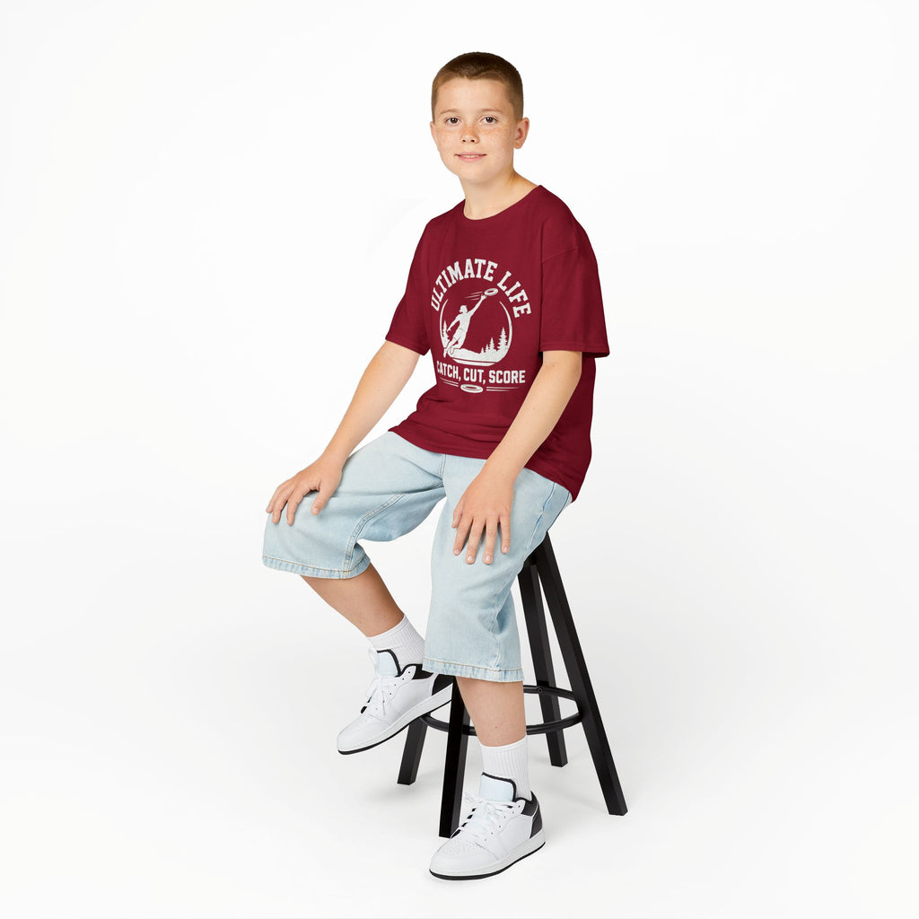 Young boy sitting on a stool wearing a red t-shirt with text and graphics, light blue jeans, and white sneakers.