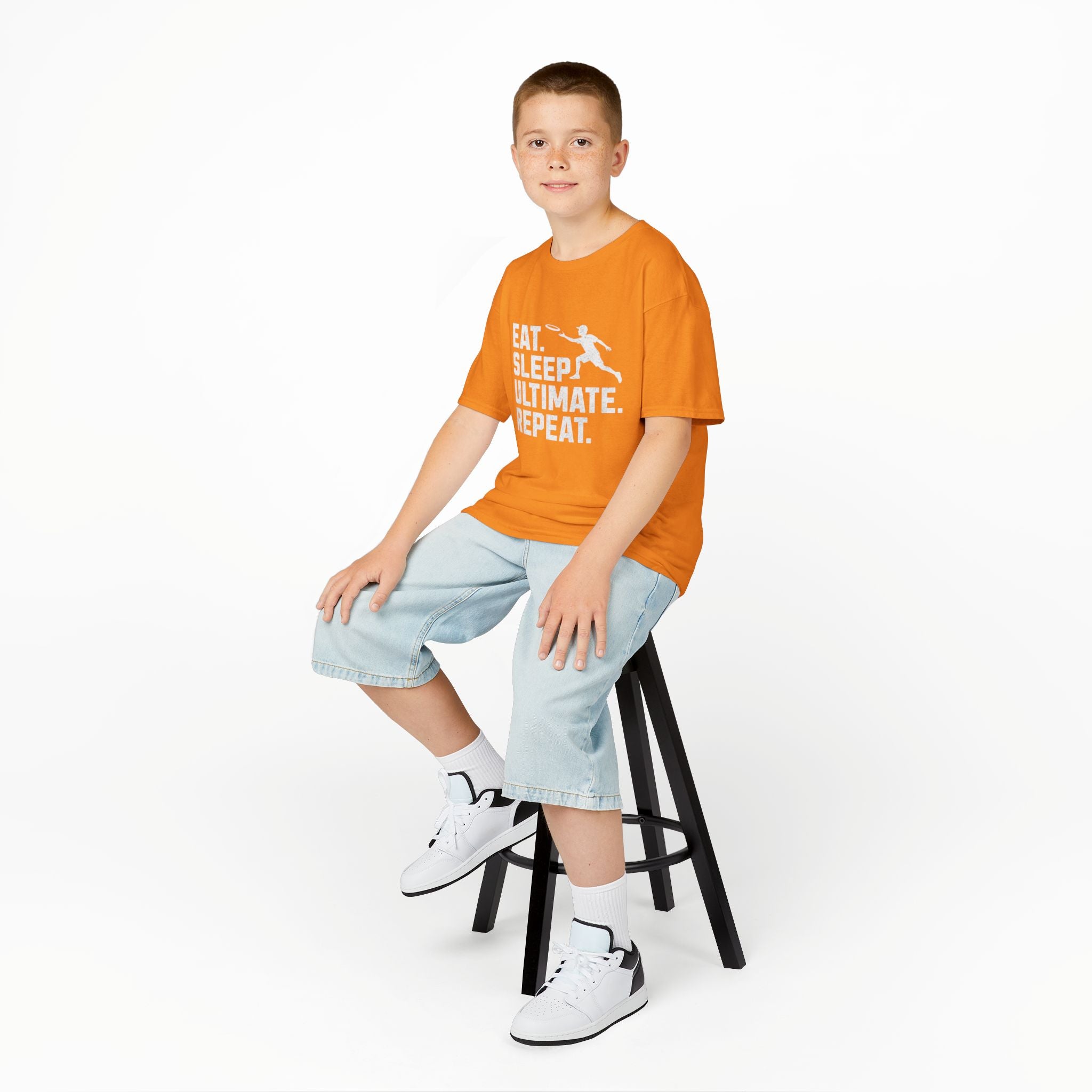 Child wearing an orange t-shirt with a logo, light blue jeans, and white sneakers on a white background