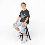 Young boy sitting on a stool wearing a black t-shirt with white text and light blue jeans.
