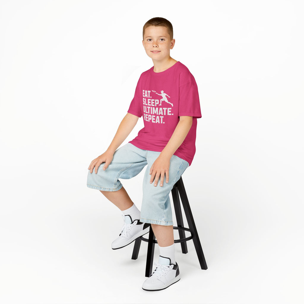 Child sitting on a stool wearing a pink t-shirt with text and light blue shorts on a white background