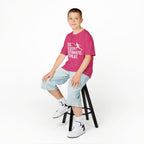 Child sitting on a stool wearing a pink t-shirt with text and light blue shorts on a white background