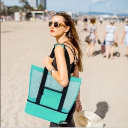 Woman holding a teal and black tote bag on a beach