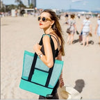 Woman holding a teal and black tote bag on a beach
