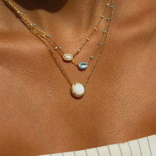 Two gold necklaces with gemstones on a brown surface
