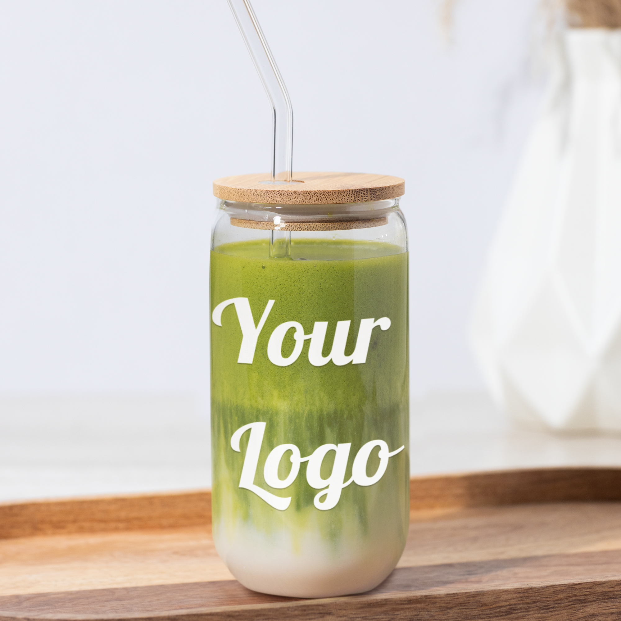 Green smoothie in a jar with a wooden lid and straw, on a wooden tray with a blurred background.