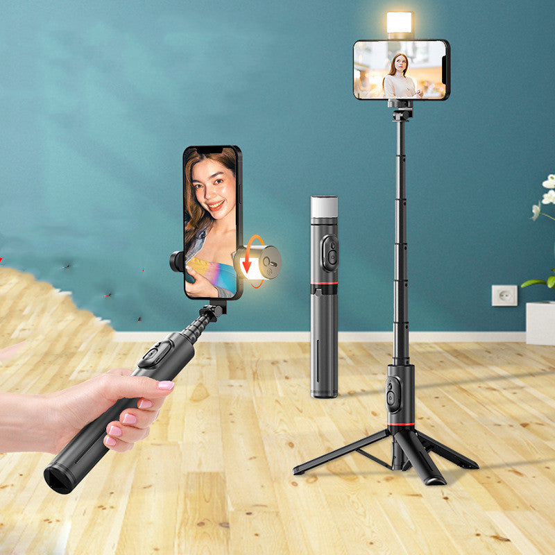 Handheld selfie stick with smartphone holder and light on a wooden floor against a blue wall.