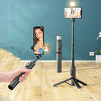 Handheld selfie stick with smartphone holder and light on a wooden floor against a blue wall.