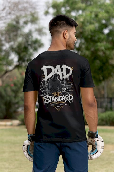 Man wearing a black t-shirt with football themed 'DAD THE STANDARD' design outdoors