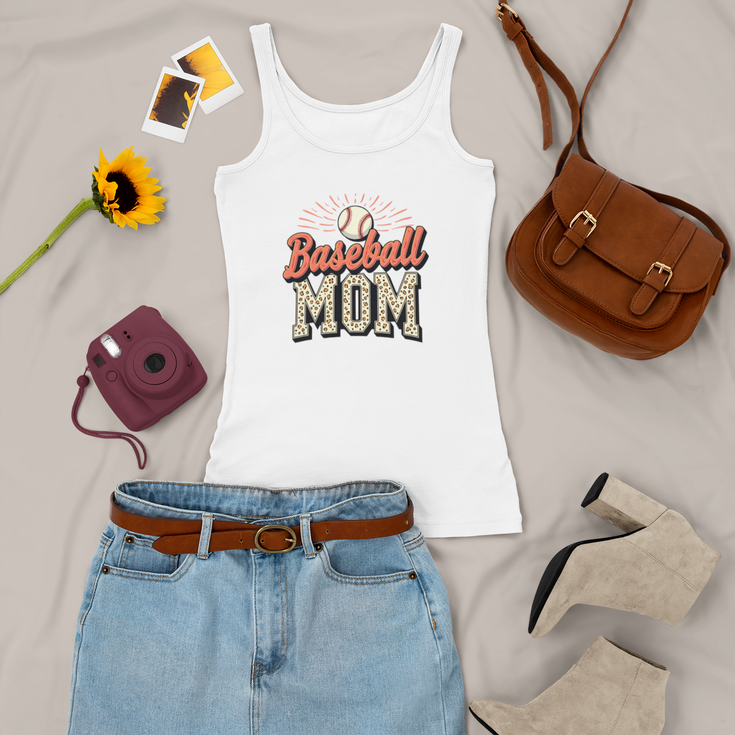 White tank top with 'Baseball Mom' text, denim skirt, brown purse, sunflower, camera, and shoes on a light gray background
