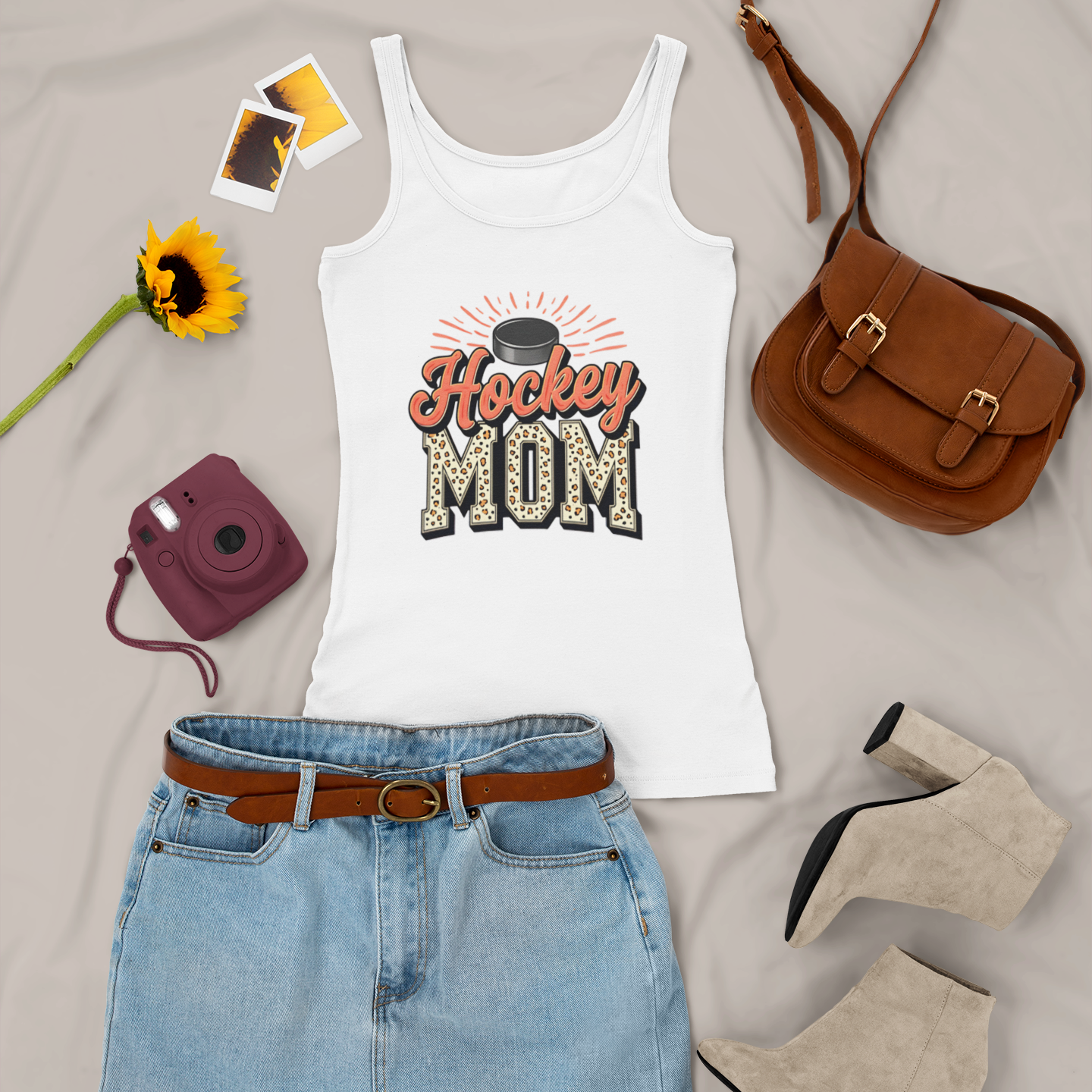White tank top with 'Hockey Mom' design, denim skirt, brown purse, sunflower, and camera on a light gray background