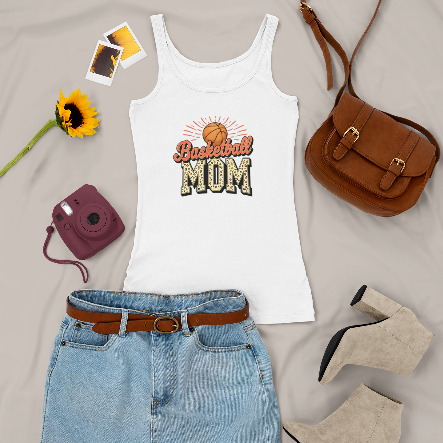 White tank top with 'Wrestling Mom' design, denim skirt, brown purse, sunflower, and camera on a light gray background